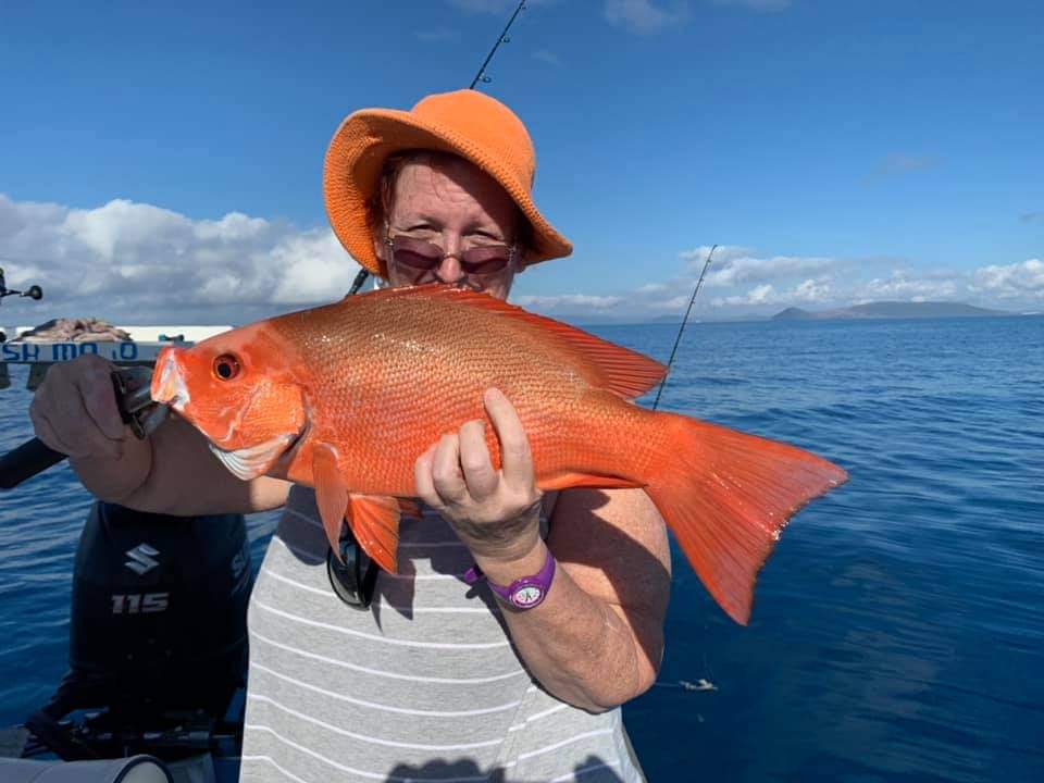 A happy angler in an orange hat with a red reef fish