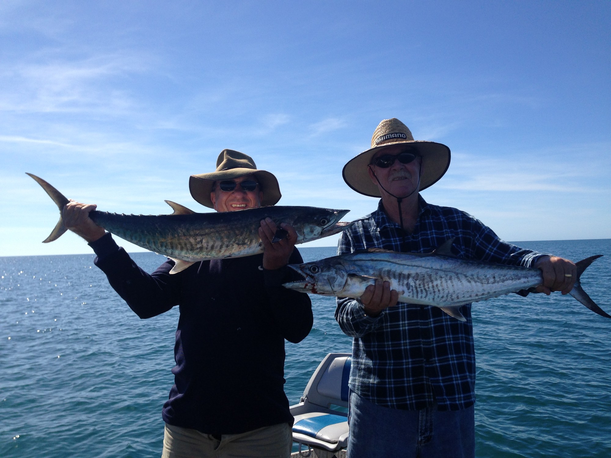 Two anglers each holding a Spanish mackerel at sea