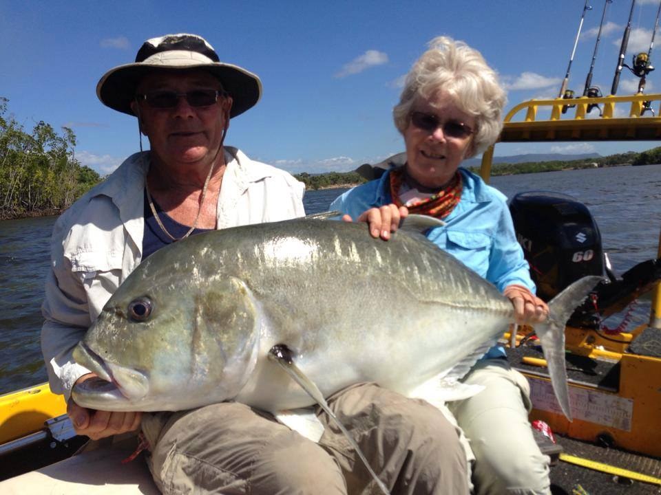Two anglers holding a giant trevally on the boat